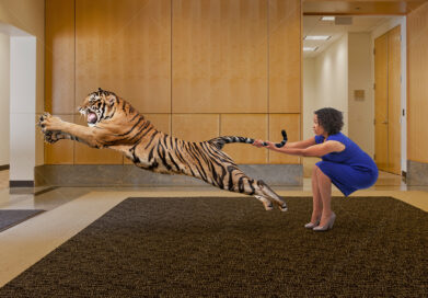 A businesswoman holds a leaping tiger by the tail in a corporate lobby.